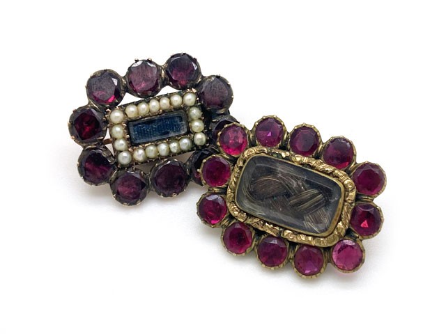 Antique Georgian garnet brooches each witha center of braided hair; one with pearls and the other with repousse border.